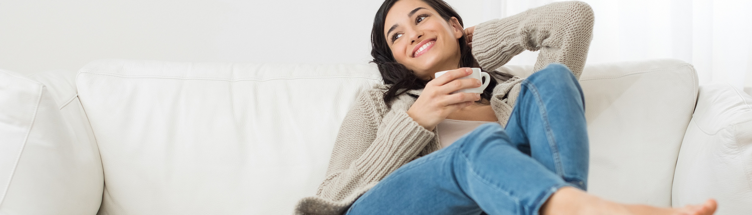Eine Frau entspannt auf dem Sofa und trinkt einen Kaffee.